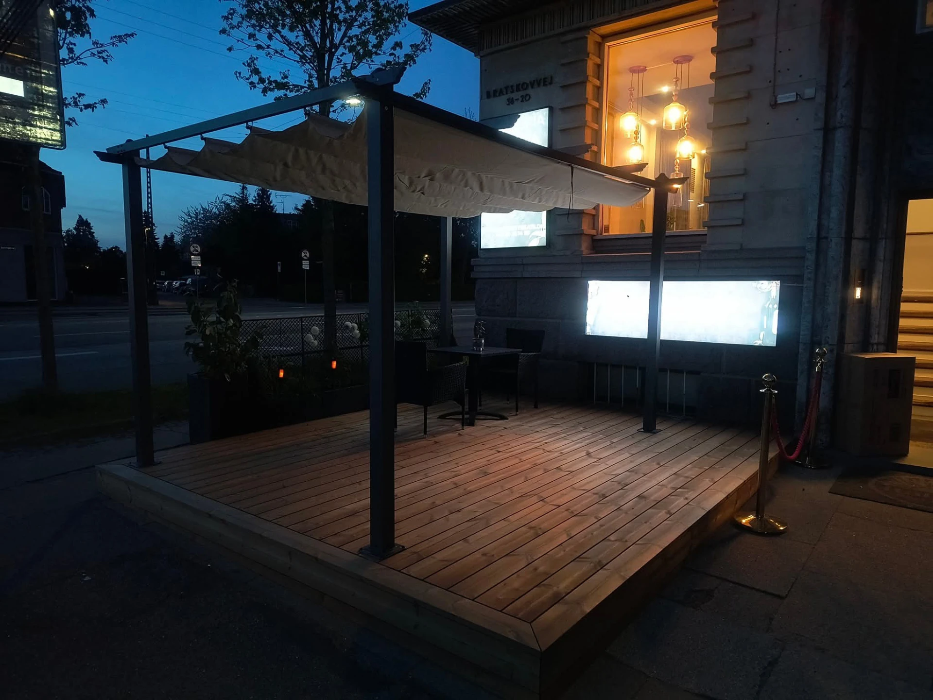 Trædæk med pergola og markise foran facade om aftenen